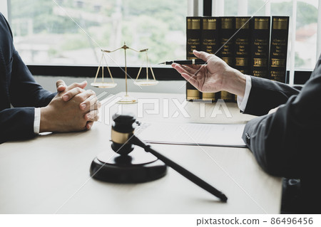 A male lawyer or a judge counseling clients about judicial justice and prosecution with scales, judges gavel, legal documents legal services concept 86496456