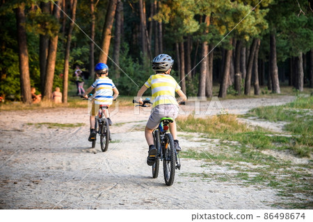 Family in the park on bicycles. two sibling brothers kids boys compete in riding. view from back Family in the park on bicycles. two sibling brothers kids boys compete in riding. view from back 86498674