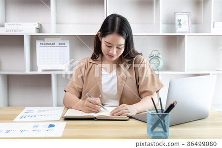 Asian woman taking notes in notebook while studying online in laptop at home, Video chat, Online communication , Stay home, New normal, Distance learning , Social distancing, Learn online. Asian woman taking notes in notebook while studying online in laptop at home, Video chat, Online communication , Stay home, New normal, Distance learning , Social distancing, Learn online. 86499080