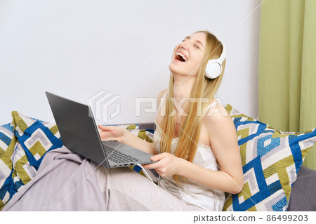 Young woman laughing while watching video on laptop at home Young woman laughing while watching video on laptop at home 86499203