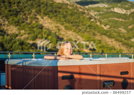 Portrait of young carefree happy smiling woman relaxing at hot tub during enjoying happy traveling moment vacation life against the background of green big mountains 86499257