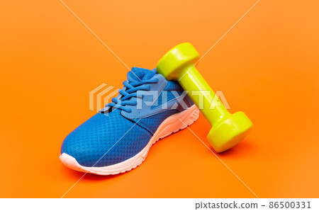 comfortable blue sport shoe with barbell on orange background, sport accessory comfortable blue sport shoe with barbell on orange background, sport accessory 86500331
