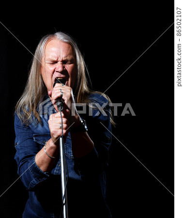 elderly man with long gray hair in blue denim shirt sings into a microphone elderly man with long gray hair in blue denim shirt sings into a microphone 86502107