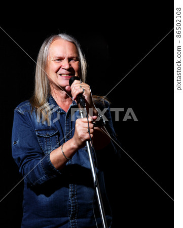 elderly man with long gray hair in blue denim shirt sings into a microphone elderly man with long gray hair in blue denim shirt sings into a microphone 86502108