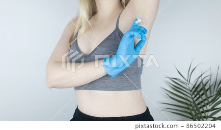 Girl in a blue medical glove smears a cream with botulinum toxin under her armpit. Novelty in cosmetology and medicine. Replacement of injection therapy. Painless treatment for excessive sweating. 86502204