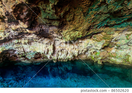 View of beautiful natural pool of crystal clear water formed in a rocky cave with stalagmites and stalagmites. Kuza cave in Zanzibar, Tanzania 86502620
