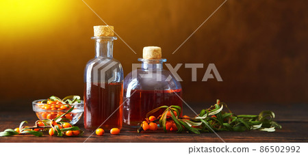 Glass bottle with sea buckthorn oil berries and sea buckthorn branches on wooden background Glass bottle with sea buckthorn oil berries and sea buckthorn branches on wooden background 86502992