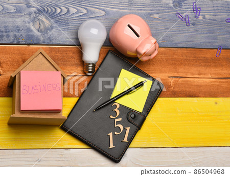 Moneybox near organizer, pen, sticky notes, idea lamp and phone Moneybox near organizer, pen, sticky notes, idea lamp and phone 86504968