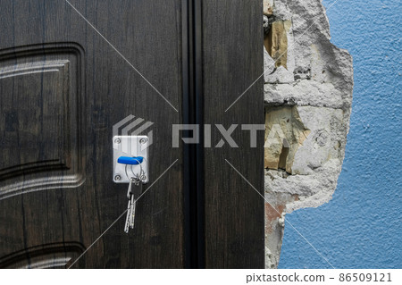 The keychain sits in the door lock as you open or close the entry or exit doors near an old broken wall in need of repair and reconstruction apartament, damaged architecture The keychain sits in the door lock as you open or close the entry or exit doors near an old broken wall in need of repair and reconstruction apartament, damaged architecture 86509121