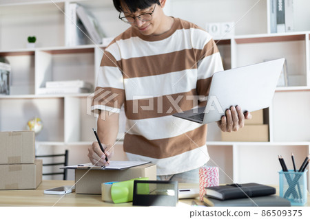 Sell online, Young man is writing down the customer's details and addresses on the notebook or box in order to prepare for shipping according to the information, Online shopping SME entrepreneur. Sell online, Young man is writing down the customer's details and addresses on the notebook or box in order to prepare for shipping according to the information, Online shopping SME entrepreneur. 86509375