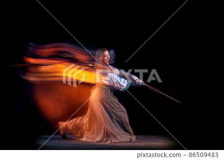 Portrait of beautiful woman in image of medieval warrior or knight with dirty wounded face with big sword isolated over dark background in mixed neon light. 86509483