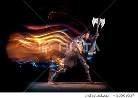 Dynamic portrait of brutal serious man, medieval knight with swinging ax fighting isolated over dark background in neon mixed light. Art, history, creativity Dynamic portrait of brutal serious man, medieval knight with swinging ax fighting isolated over dark background in neon mixed light. Art, history, creativity 86509534