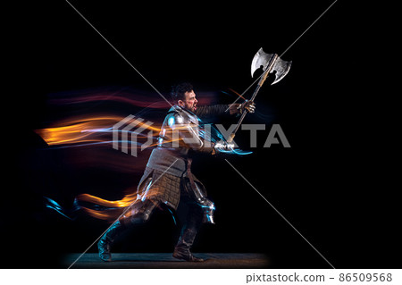 Dynamic portrait of brutal serious man, medieval knight with swinging ax fighting isolated over dark background in neon mixed light. Art, history, creativity Dynamic portrait of brutal serious man, medieval knight with swinging ax fighting isolated over dark background in neon mixed light. Art, history, creativity 86509568