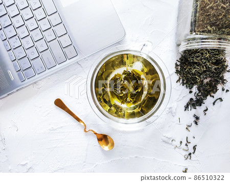 Office desk with glass cup of green tea and laptop Office desk with glass cup of green tea and laptop 86510322