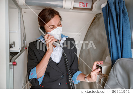 Woman stewardess in face mask talking on telephone in airplane 86511941