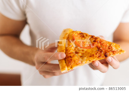 Close-up of unrecognizable man wearing white clothes holding in hands piece of appetizing pizza on white isolated background, studio shot, selective focus. 86513005