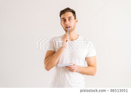 Studio portrait of thoughtful young man writing in copybook touching chin on white isolated background. Pensive male student studying, preparing for exam, making notes in paper notebook. Studio portrait of thoughtful young man writing in copybook touching chin on white isolated background. Pensive male student studying, preparing for exam, making notes in paper notebook. 86513051