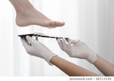 Orthopedic insole on a white background. Hands in rubber gloves hold an orthopedic insole. Foot care, comfort for the feet. Doctor orthopedist tests the medical device. Flat feet correction. Orthopedic insole on a white background. Hands in rubber gloves hold an orthopedic insole. Foot care, comfort for the feet. Doctor orthopedist tests the medical device. Flat feet correction. 86513199