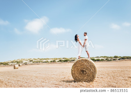 Couple in love in the field. Man and woman near a haystack.  Round haystack. A man and a woman standing near a haystack. Couple travels. Honeymoon. Newly married couple. Man and woman holding hands 86513531