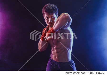 Front view of muscular kickboxer who delivering elbow hit isolated on smoke background. Mixed media 86513627