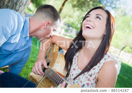 Young Adult Girl Playing Guitar with Boyfriend In The Park. 86514287