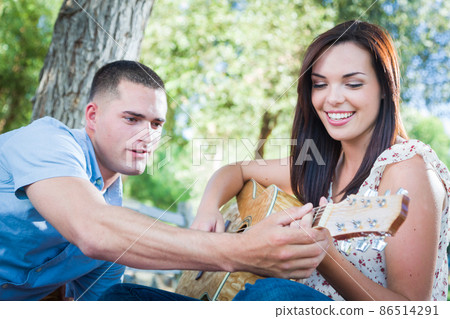 Young Adult Man Teaching Girlfriend How To Play The Guitar Outside in the Park. 86514291