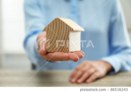 Real estate agent holding house figure at wooden table, closeup Real estate agent holding house figure at wooden table, closeup 86516243