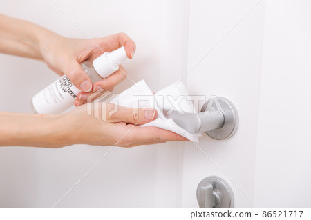 Cleaning white door handles with an antiseptic wet wipe and sanitizer spray. Disinfection in hospital and public spaces against corona virus. Woman hand using towel for cleaning home room door link. Cleaning white door handles with an antiseptic wet wipe and sanitizer spray. Disinfection in hospital and public spaces against corona virus. Woman hand using towel for cleaning home room door link. 86521717