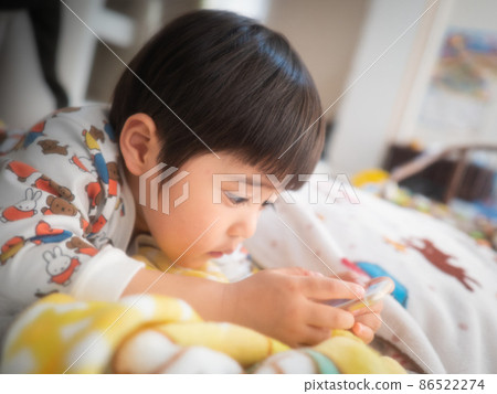 A 3-year-old child lying down and playing with his smartphone 86522274