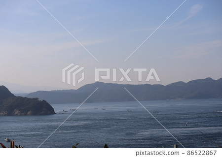 藍天白雲薄雲對岸的陸山，有白色燈塔的半島，蔚藍的海面上有許多漁船的海景 86522867