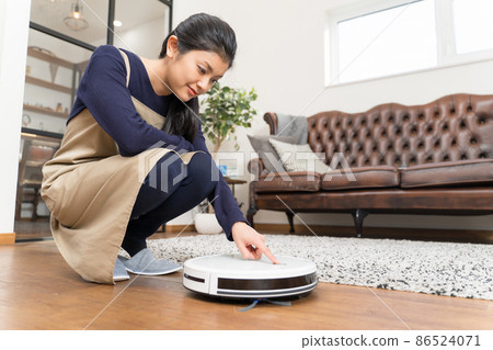 Young woman pushing a switch on a robot vacuum 86524071