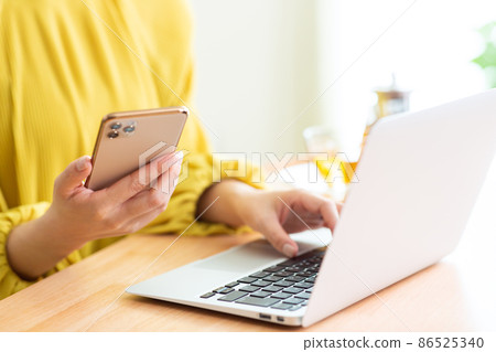 一個在客廳裡使用電腦和智能手機的女人。 86525340