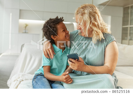 Smiling African American child boy and her mom sitting on couch, relaxing and playing Smiling African American child boy and her mom sitting on couch, relaxing and playing 86525516