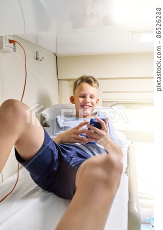 Blond boy reads book with phone lying on top bed in train 86526288