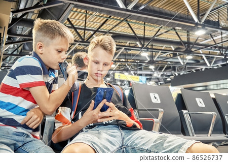 Brothers play games on phones sitting in airport hall 86526737