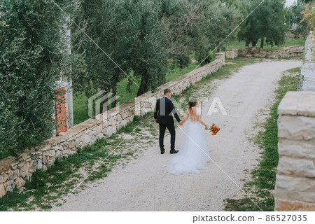 Happy stylish smiling couple walking in Tuscany, Italy on their wedding day. The bride and groom walk down the street by the hands. A stylish young couple walks. Husband and wife communicate nicely Happy stylish smiling couple walking in Tuscany, Italy on their wedding day. The bride and groom walk down the street by the hands. A stylish young couple walks. Husband and wife communicate nicely 86527035