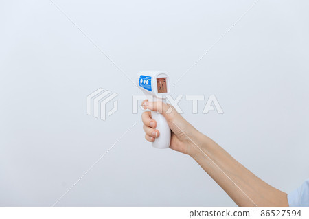 Temperature measurement gun in doctor hands. Close-up shot of doctor wearing protective surgical mask ready to use infrared isometric thermometer gun to check body temperature for virus symptoms. 86527594