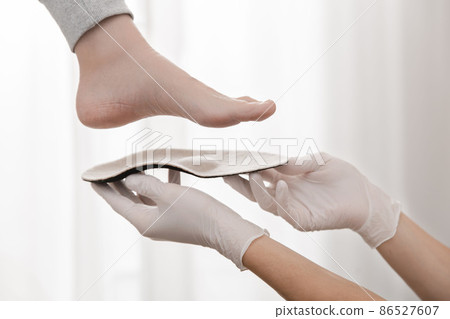 Orthopedic insole on a white background. Hands in rubber gloves hold an orthopedic insole. Foot care, comfort for the feet. Doctor orthopedist tests the medical device. Flat feet correction. Orthopedic insole on a white background. Hands in rubber gloves hold an orthopedic insole. Foot care, comfort for the feet. Doctor orthopedist tests the medical device. Flat feet correction. 86527607