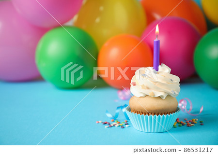 Birthday cupcake with candle and blurred balloons on background. Space for text 86531217