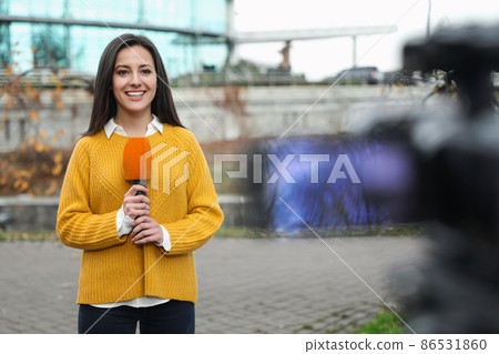Young female journalist with microphone working on city street Young female journalist with microphone working on city street 86531860