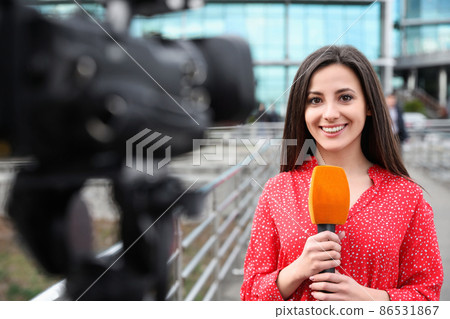 Young female journalist with microphone working on city street 86531867