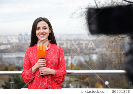 Young female journalist with microphone working on city street 86531868