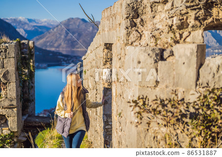 Young tourist woman enjoying a view of Kotor Bay, Montenegro. Kotor Old Town Ladder of Kotor Fortress Hiking Trail. Aerial drone view 86531887
