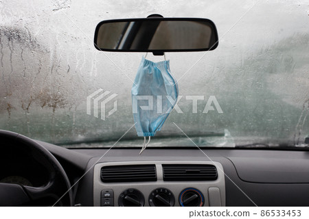 Surgical mask hanging from a car mirror. The pandemic and depression, concept 86533453