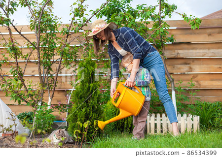 Child and mother watering can watering a garden in the backyard 86534399