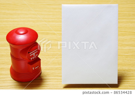Postbox-shaped piggy bank and postal envelope placed on a wooden desk (with copy space) 86534428