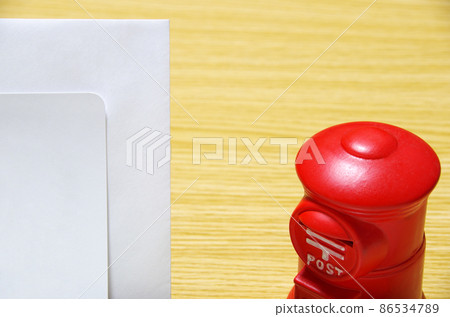Postbox-shaped piggy bank and thank-you note envelope placed on a wooden desk (with copy space) 86534789