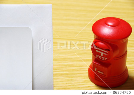Postbox-shaped piggy bank and thank-you note envelope placed on a wooden desk (with copy space) 86534790