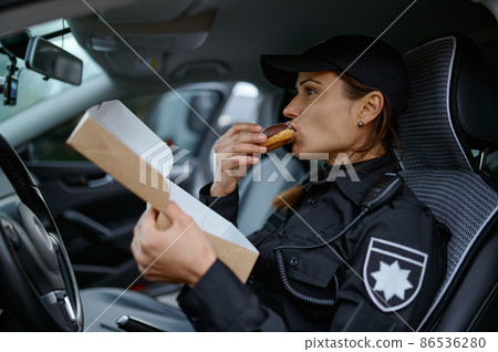 Woman police officer eating donut in car 86536280