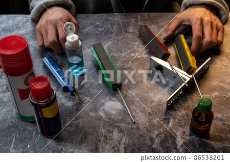 Hands of a knife sharpener. Tools for sharpening knives and scissors. Grinder and oil. Hands of a knife sharpener. Tools for sharpening knives and scissors. Grinder and oil. 86538201